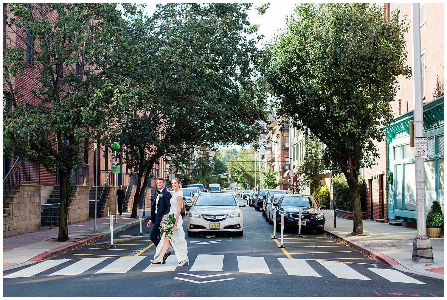 bride and groom walk across city street surrounded by trees