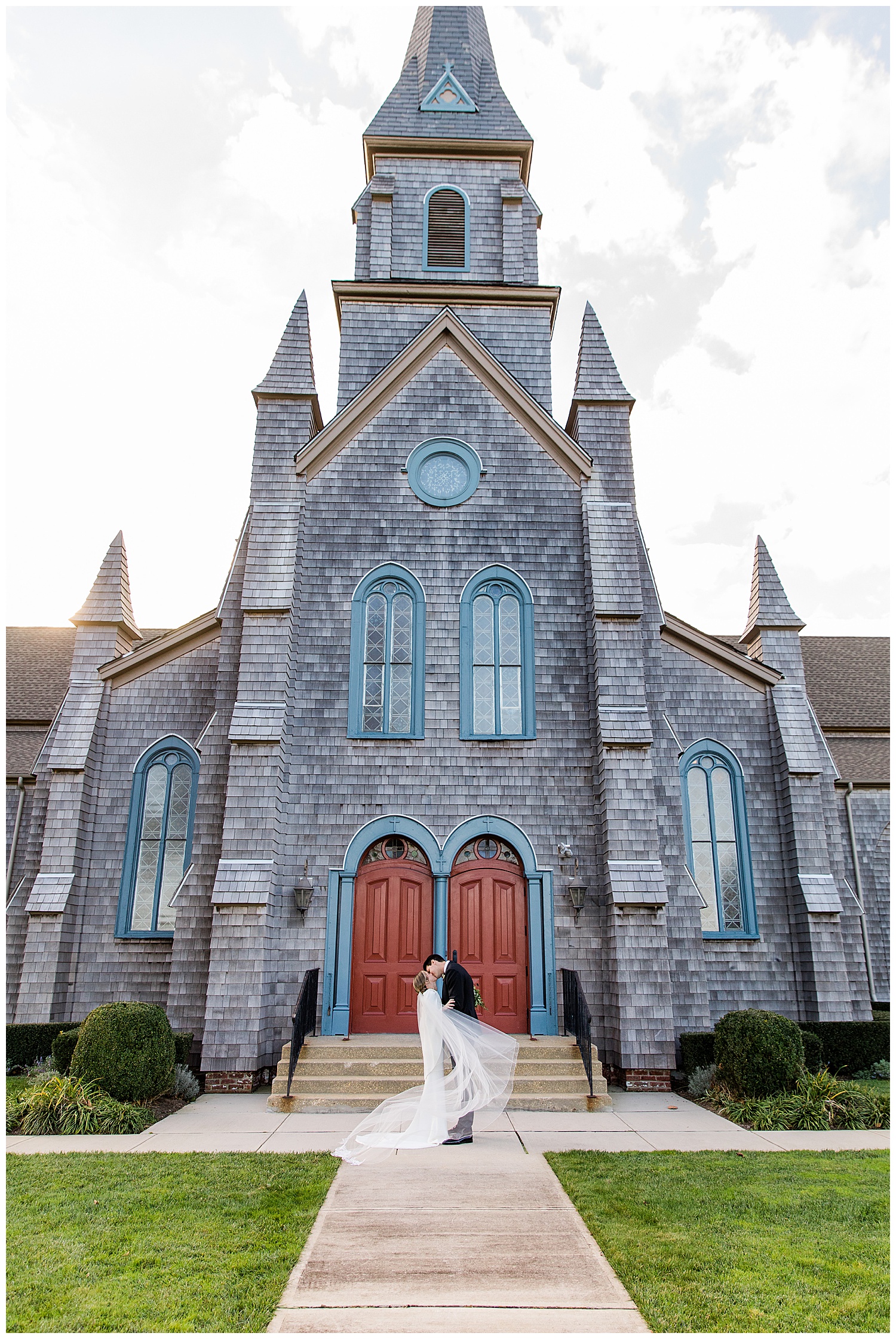 bride and groom kiss in front of tall stone church with red doors