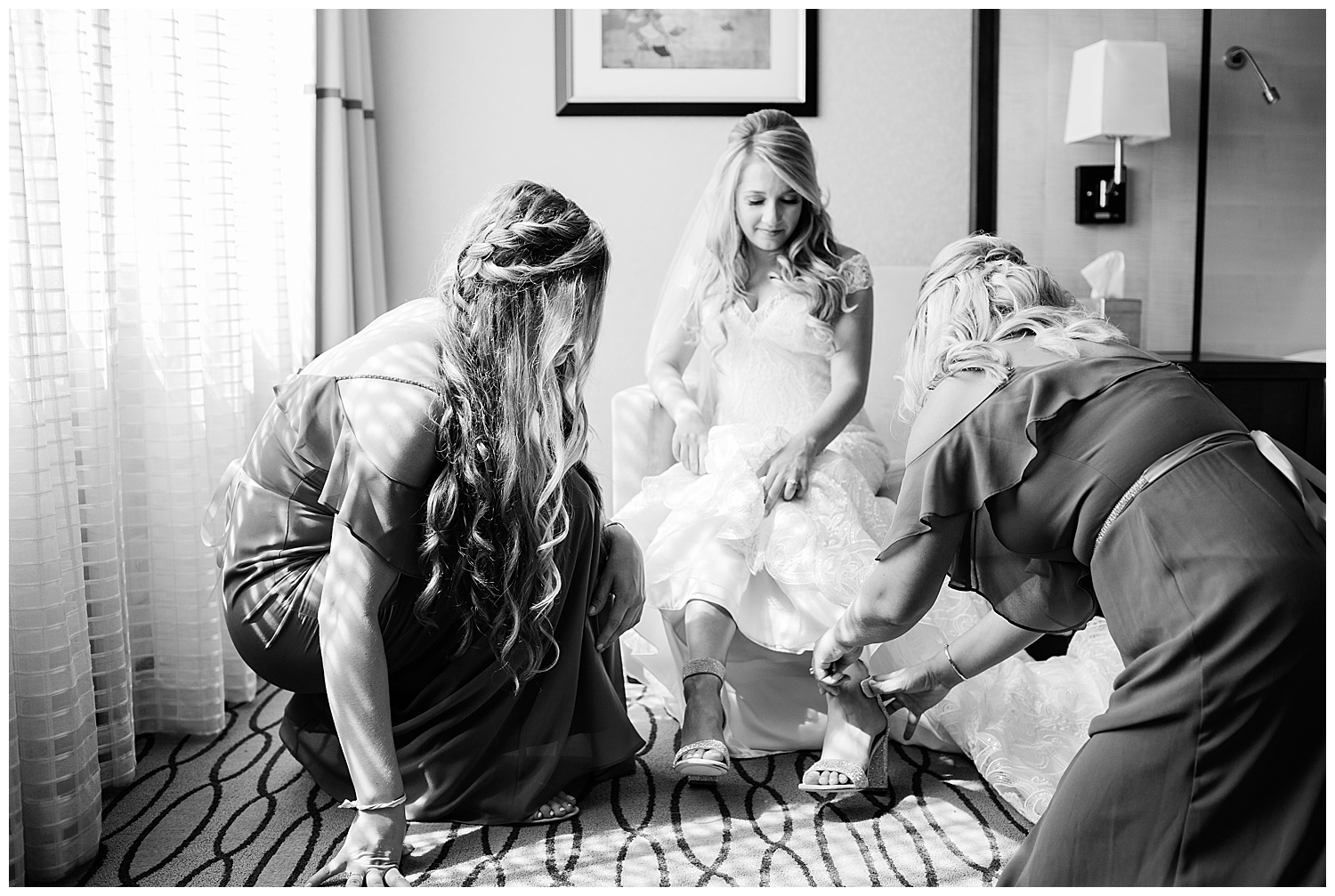 bride's mother helps her put on her shoes while she holds her skirt