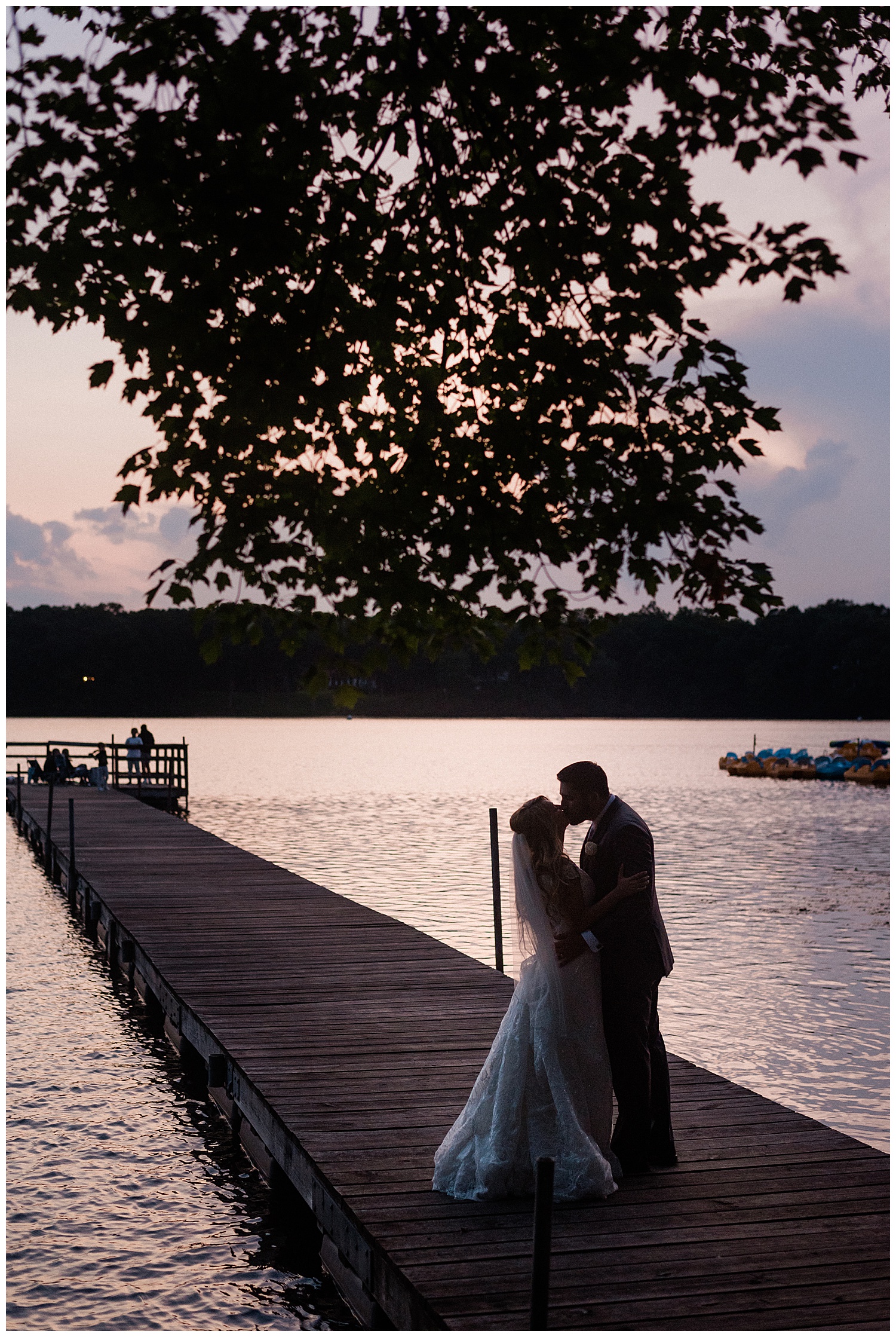 bride and groom kiss under tree on a lake at sunset