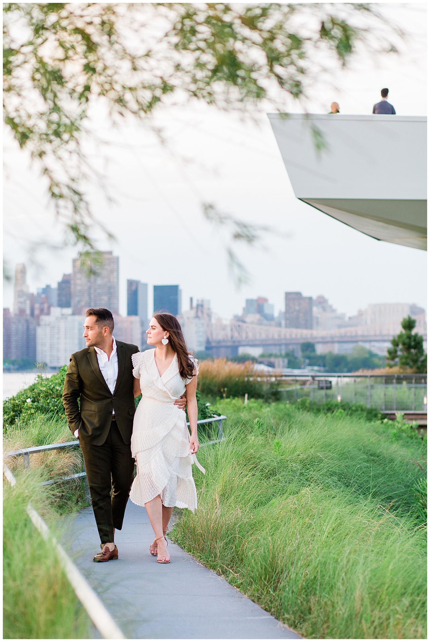 Couple walk along park path in front of city skyline