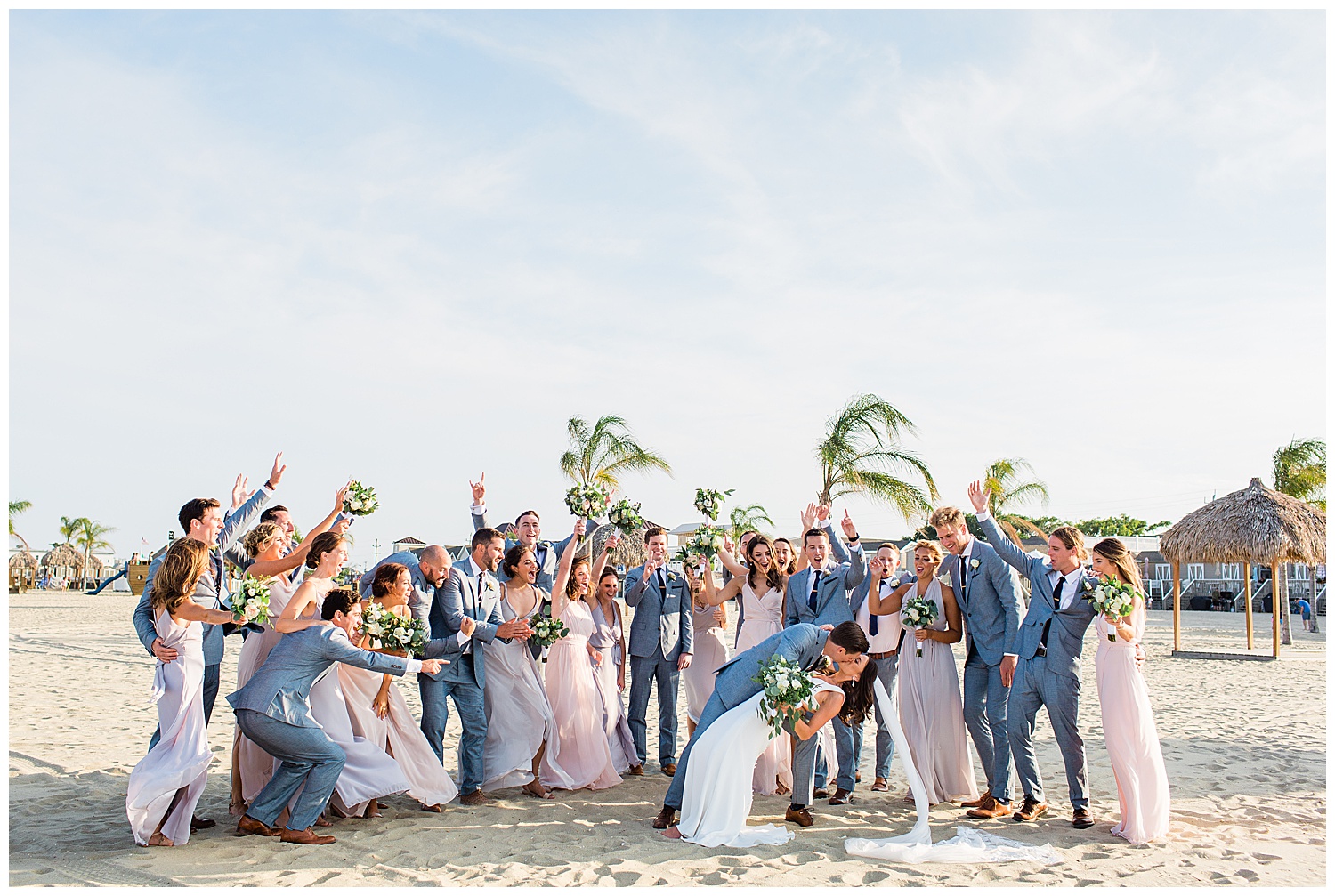bridal party celebrates while groom kisses bride at beach wedding in Sea Bright, New Jersey