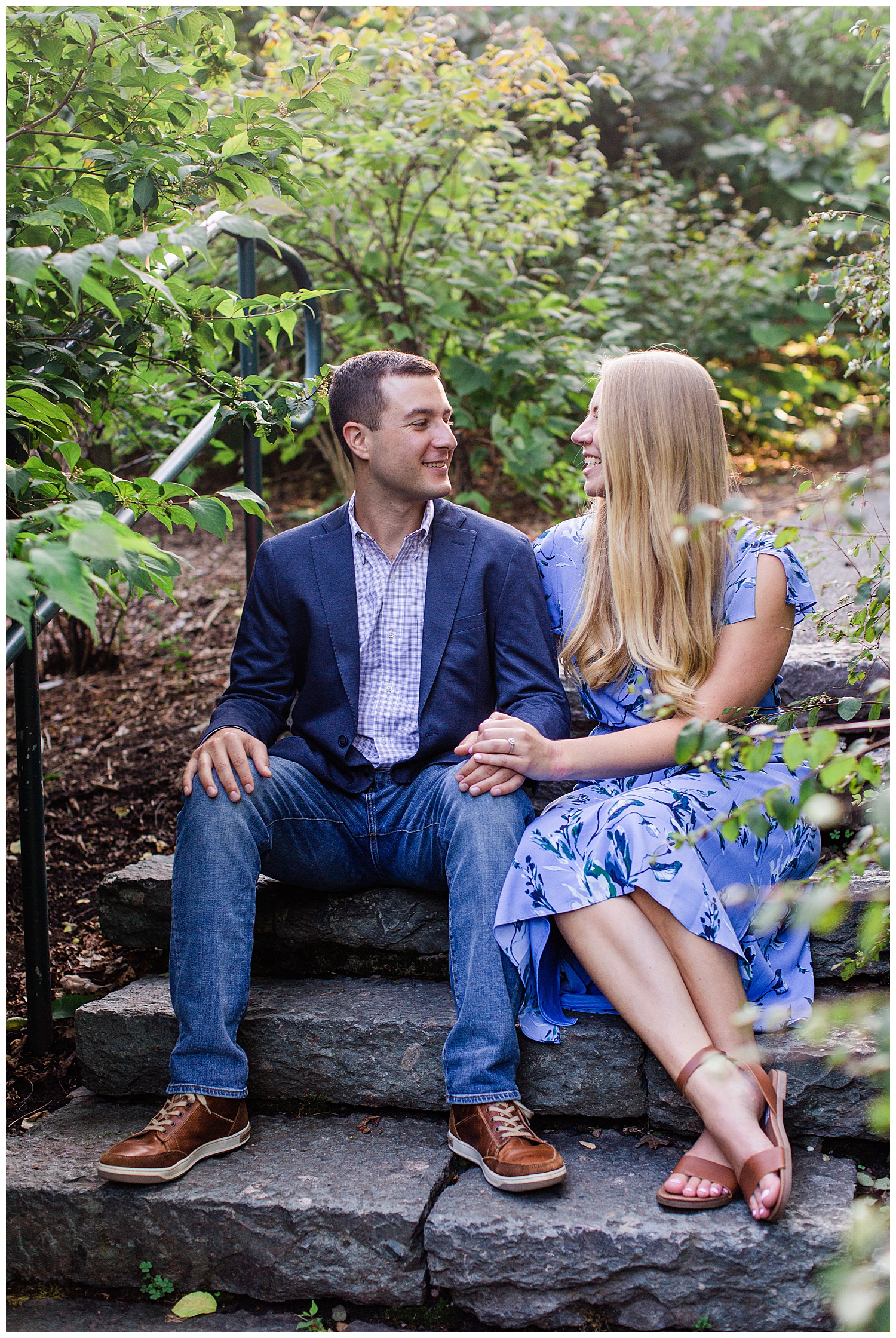 Couple laughs together on stone steps surrounded by greenery