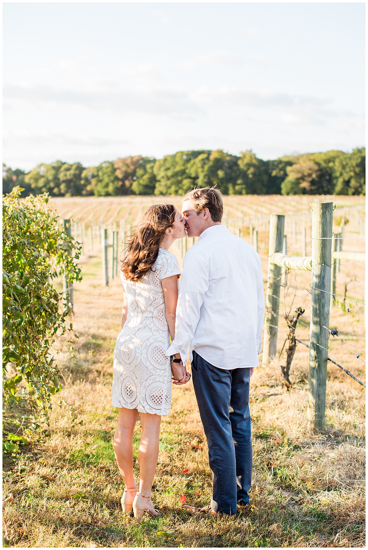 Couple kiss in the winery with a field behind them